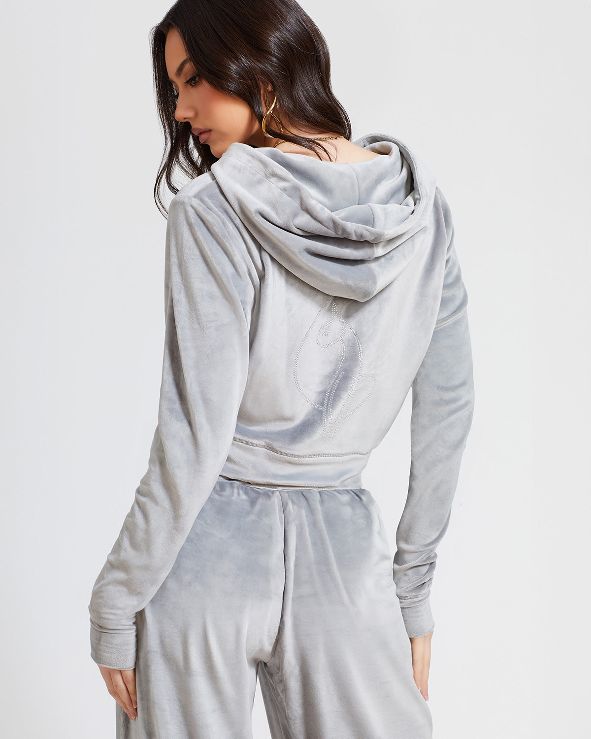 Back view image of standard sized model shown wearing grey velour zip up hoodie with matching wide leg sweatpants. Zippered sweatshirt features rhinestone Baby Phat script logo on upper chest and oversized rhinestone cat logo on the back. Sweatshirt features silver cat logo zipper pull.