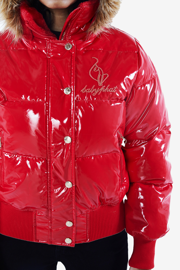 Baby Phat reissue OG puffer jacket in gloss red is a glossy red lacquer jacket that features a faux fur trim hood, cat logo detailing on the front and back, gold buttons, and a cat zipper pull.