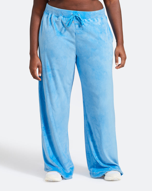 Plus sized model shown wearing blue velour sweatpants. Pants feature a wide leg, open bottom fit with a rhinestone Baby Phat cat logo on the wearer's left upper thigh. Pants feature pockets and an elastic waistband with a drawstring tie.