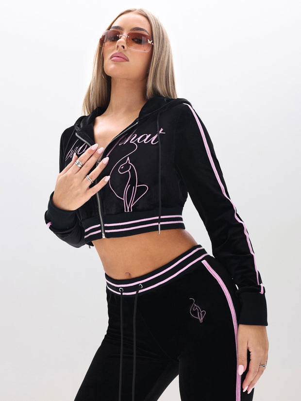 A woman poses confidently in a Velour Hoodie with Embroidery, featuring black and pink colors and cat designs, styled with sunglasses and manicured nails against a plain background.
