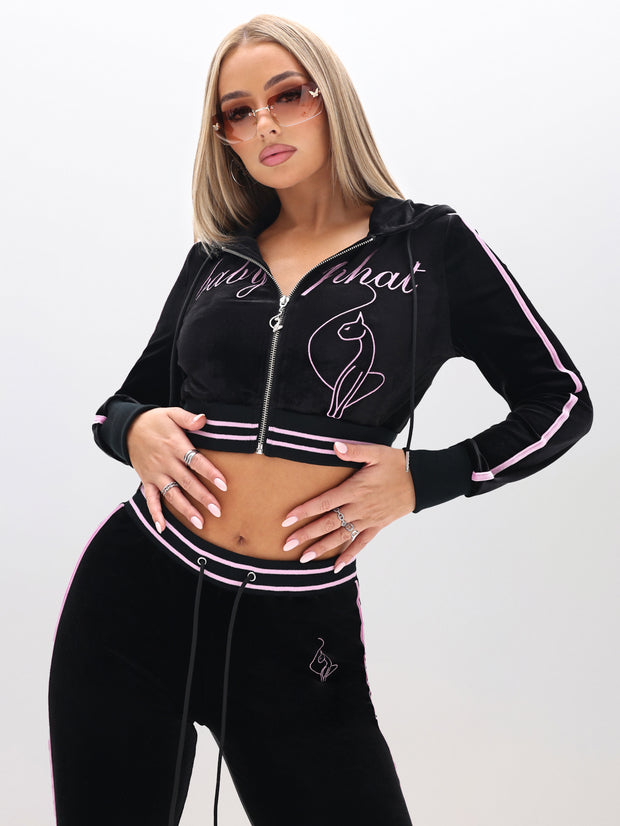 Woman in a Velour Hoodie with Embroidery, black with pink stripes and cat detail, sunglasses, and long straight hair, standing against a plain white background.