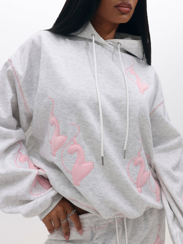 A woman wears the Logo Marled Hoodie in light gray with white drawstrings and pink abstract flame designs, paired with matching shorts.