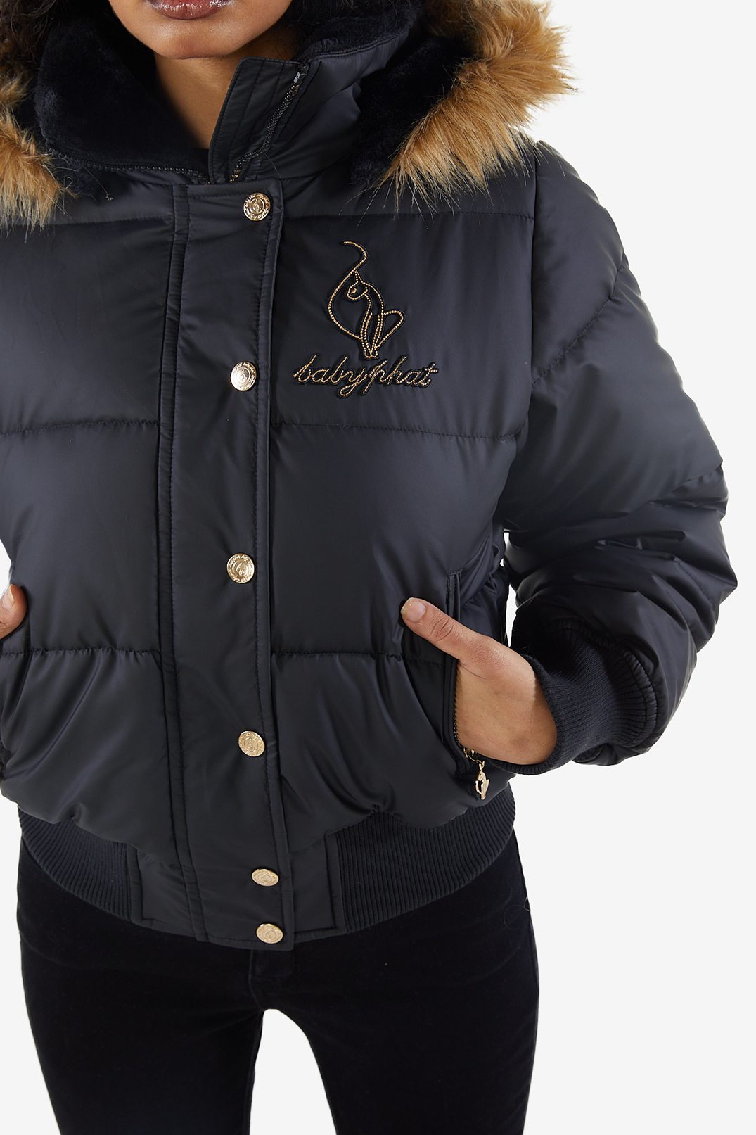 Baby Phat reissue OG puffer jacket in onyx is a matte black jacket that features a faux fur trim hood, cat logo detailing on the front and back, gold buttons, and a cat zipper pull.
