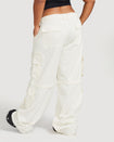 Back view image of plus sized model’s legs wearing off white cargo pant with visible belt loops. Pants feature exaggerated pocket detailing down both legs and large pockets on both sides of rear. Hidden zippers below the knees. 