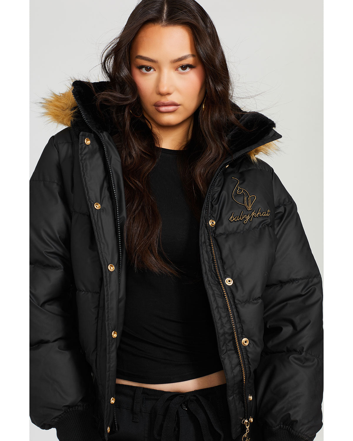 Model shown wearing black puffer jacket. Coat features natural faux fur trimmed detachable hood and Baby Phat script logo on front chest and oversized cat logo on the back. Jacket also features gold cat logo zipper pulls on the front pockets and center front.