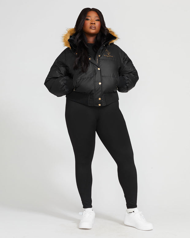 Plus sized model shown wearing black puffer jacket. Coat features natural faux fur trimmed detachable hood and Baby Phat script logo on front chest and oversized cat logo on the back. Jacket also features gold cat logo zipper pulls on the front pockets and center front.