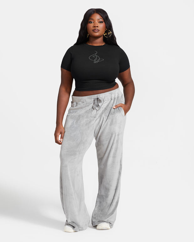 Plus sized model shown wearing grey velour sweatpants. Pants feature a wide leg, open bottom fit with a rhinestone Baby Phat cat logo on the wearer's left upper thigh. Pants feature pockets and an elastic waistband with a drawstring tie. Model is shown wearing a black t-shirt with rhinestone cat logo on center front.