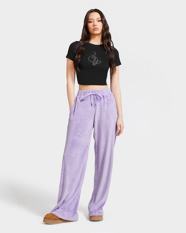 Standard sized model shown wearing light purple velour sweatpants. Pants feature a wide leg, open bottom fit with a rhinestone Baby Phat cat logo on the wearer's left upper thigh. Pants feature pockets and an elastic waistband with a drawstring tie. Model is also wearing a black t-shirt with rhinestone cat logo on center front.