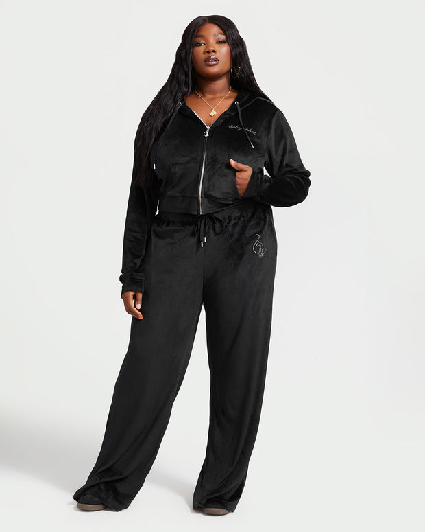 Plus sized model shown wearing black velour sweatpants. Pants feature a wide leg, open bottom fit with a rhinestone Baby Phat cat logo on the wearer's left upper thigh. Pants feature pockets and an elastic waistband with a drawstring tie.