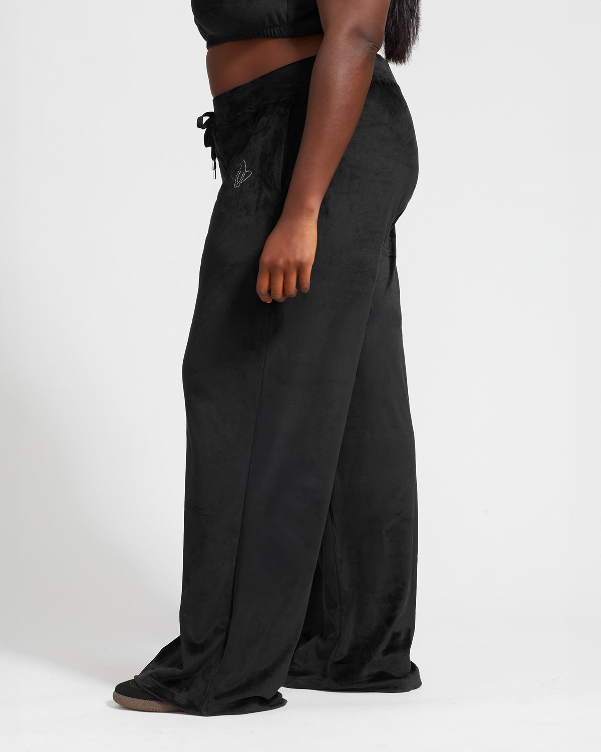 Plus sized model shown wearing black velour sweatpants. Pants feature a wide leg, open bottom fit with a rhinestone Baby Phat cat logo on the wearer's left upper thigh. Pants feature pockets and an elastic waistband with a drawstring tie.