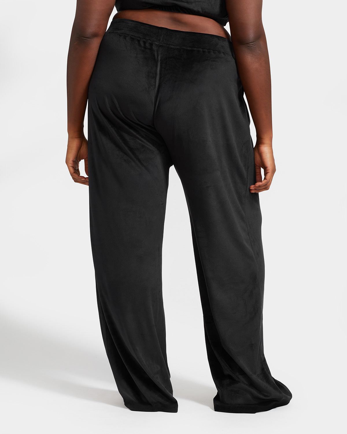 Plus sized model shown wearing black velour sweatpants. Pants feature a wide leg, open bottom fit with a rhinestone Baby Phat cat logo on the wearer's left upper thigh. Pants feature pockets and an elastic waistband with a drawstring tie.