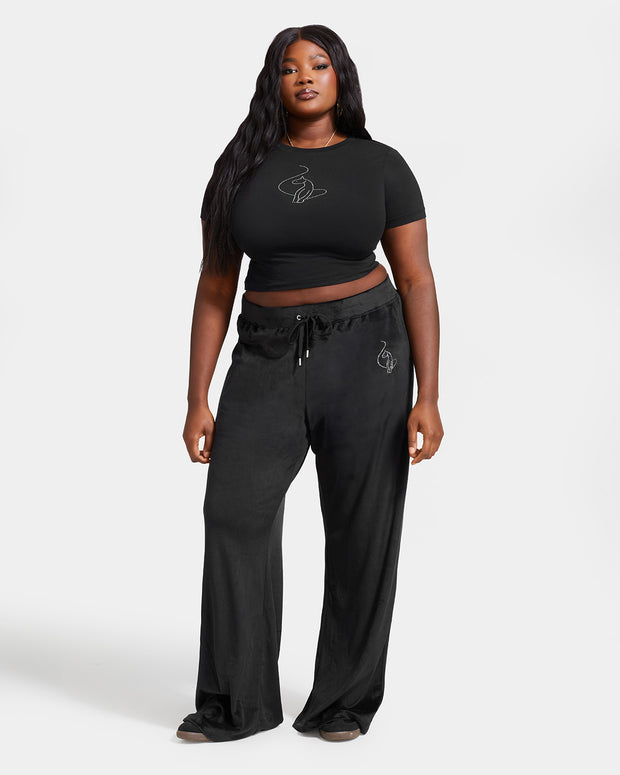 Plus sized model shown wearing black velour sweatpants. Pants feature a wide leg, open bottom fit with a rhinestone Baby Phat cat logo on the wearer's left upper thigh. Pants feature pockets and an elastic waistband with a drawstring tie.