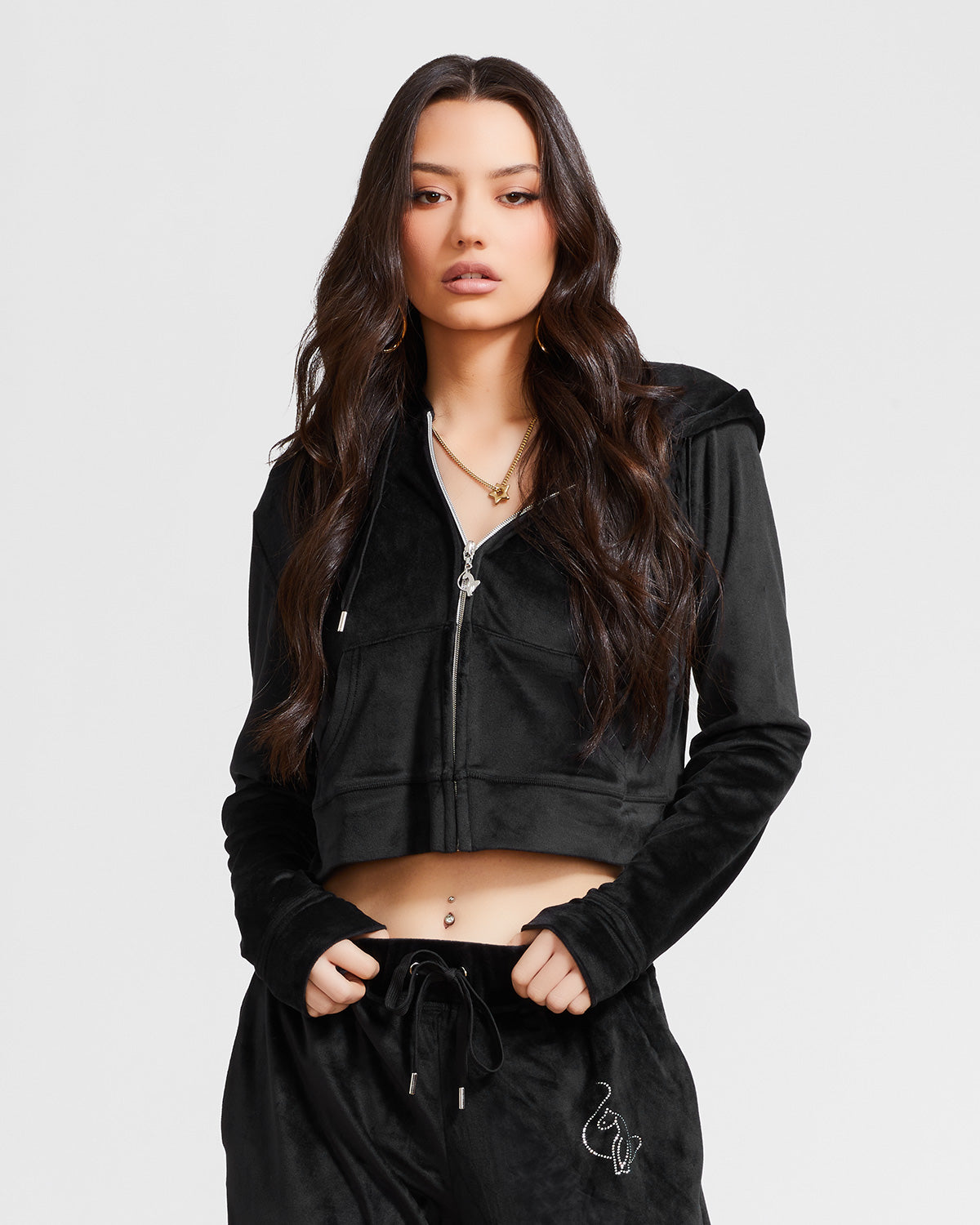 Standard sized model shown wearing black velour zip up hoodie with matching wide leg sweatpants. Zippered sweatshirt features rhinestone Baby Phat script logo on upper chest and oversized rhinestone cat logo on the back. Sweatshirt features silver cat logo zipper pull.