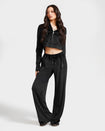 Full length image of standard sized model shown wearing black velour zip up hoodie with matching wide leg sweatpants. Zippered sweatshirt features rhinestone Baby Phat script logo on upper chest and oversized rhinestone cat logo on the back. Sweatshirt features silver cat logo zipper pull.
