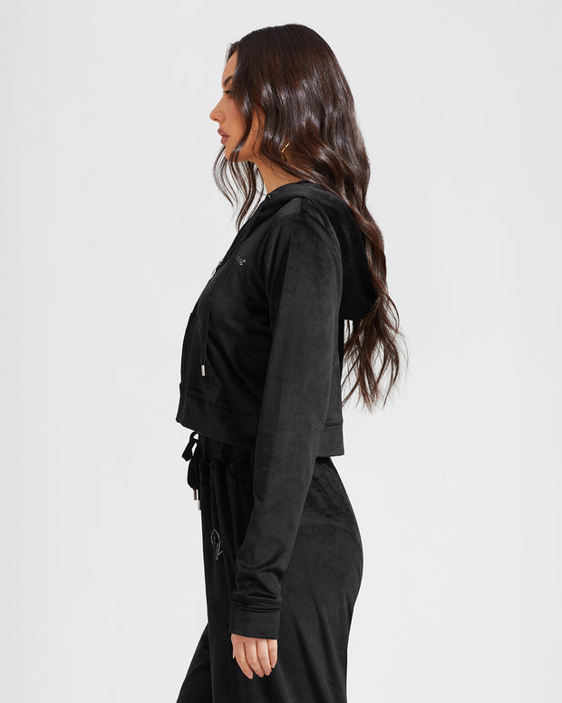 Size view image of standard sized model shown wearing black velour zip up hoodie with matching wide leg sweatpants. Zippered sweatshirt features rhinestone Baby Phat script logo on upper chest and oversized rhinestone cat logo on the back. Sweatshirt features silver cat logo zipper pull.