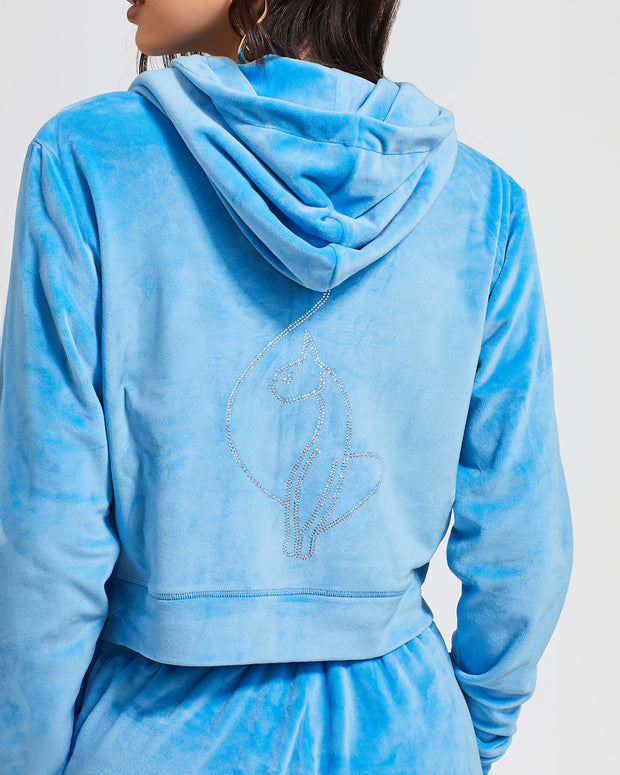 Back view image of standard sized model shown wearing blue velour zip up hoodie with matching wide leg sweatpants. Zippered sweatshirt features rhinestone Baby Phat script logo on upper chest and oversized rhinestone cat logo on the back. Sweatshirt features silver cat logo zipper pull.
