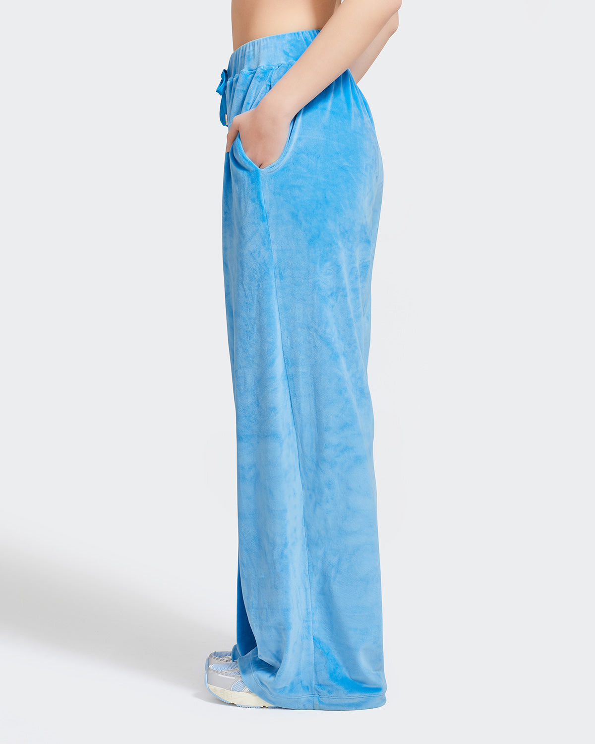 Side view image of standard sized model shown wearing blue velour sweatpants. Pants feature a wide leg, open bottom fit with a rhinestone Baby Phat cat logo on the wearer's left upper thigh. Pants feature pockets and an elastic waistband with a drawstring tie.