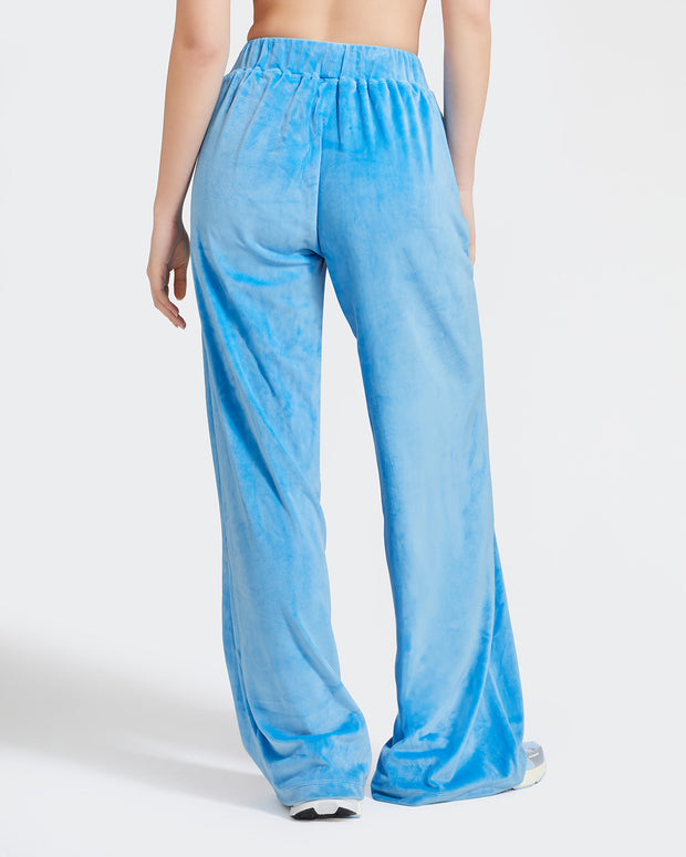 Back view image of standard sized model shown wearing blue velour sweatpants. Pants feature a wide leg, open bottom fit with a rhinestone Baby Phat cat logo on the wearer's left upper thigh. Pants feature pockets and an elastic waistband with a drawstring tie.