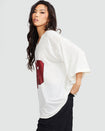 Side view image of standard sized model wearing off white oversized jersey with clear rhinestones all over. Jersey features burgundy 99 cat logo large at center front with burgundy all over rhinestones.  Jersey features v-neckline. Model is also wearing black cargo pants.