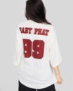 Back view image shows standard sized model wearing off white oversized jersey with clear rhinestones all over. Jersey features burgundy 99 logo large at center back with burgundy rhinestones. Jersey features large burgundy Baby Phat varsity logo across upper back.