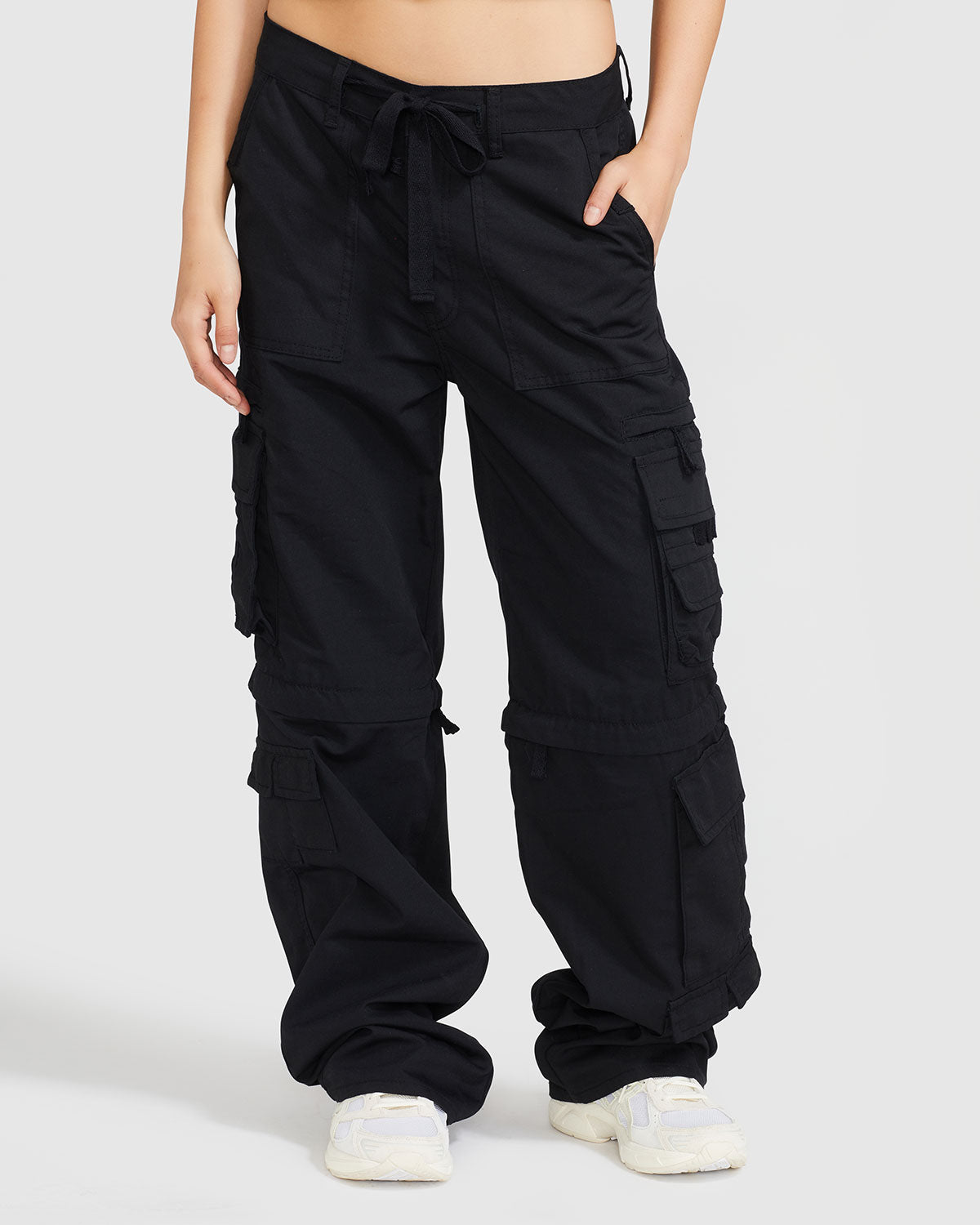 Standard sized model’s legs shown wearing black cargo pant with tied waist and belt loops. Pants feature exaggerated pocket detailing down both legs and hidden zippers below the knees. 