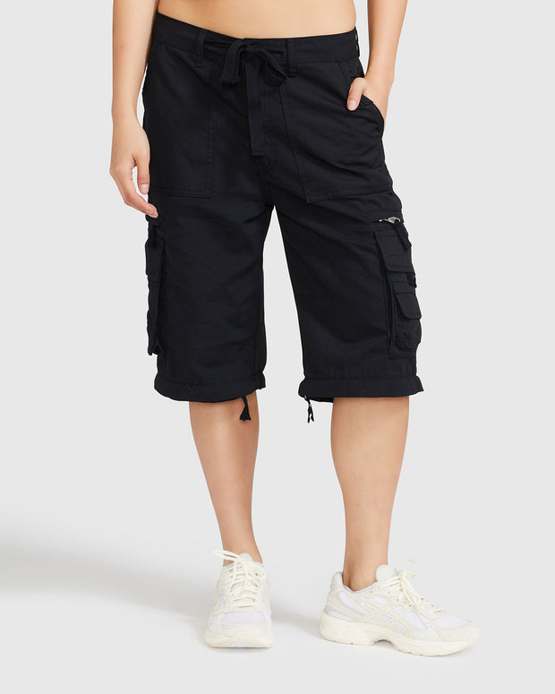 Front view image of standard sized model’s legs wearing black cargo short with visible belt loops and tied waist. Shorts feature exaggerated pocket detailing down both legs.