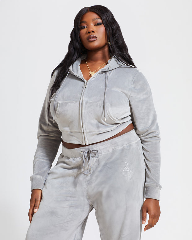 Plus sized model shown wearing grey velour zip up hoodie with matching wide leg sweatpants. Zippered sweatshirt features rhinestone Baby Phat script logo on upper chest and oversized rhinestone cat logo on the back. Sweatshirt features silver cat logo zipper pull.