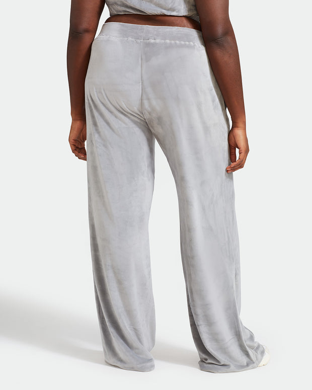 Back view image of plus sized model shown wearing grey velour sweatpants. Pants feature a wide leg, open bottom fit with a rhinestone Baby Phat cat logo on the wearer's left upper thigh. Pants feature pockets and an elastic waistband with a drawstring tie.
