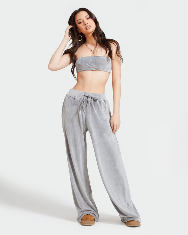 Full length image of standard sized model shown wearing grey velour sweatpants. Pants feature a wide leg, open bottom fit with a rhinestone Baby Phat cat logo on the wearer's left upper thigh. Pants feature pockets and an elastic waistband with a drawstring tie. Model is shown wearing matching grey velour bandeau.