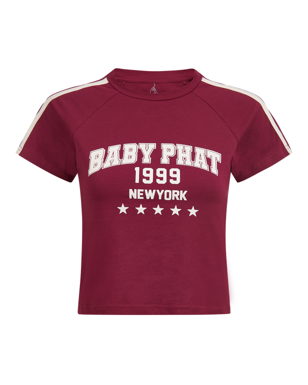 Baby Phat heritage t-shirt in burgundy features graphic cream logo with year 1999, New York, and stars. Sleeve features cream stripes.