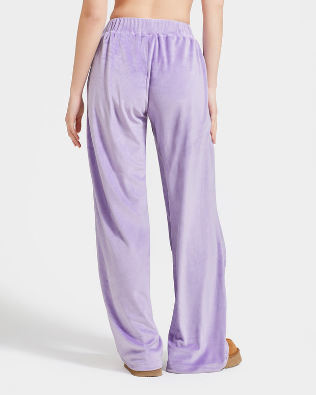 Back view image of standard sized model shown wearing light purple velour sweatpants. Pants feature a wide leg, open bottom fit with a rhinestone Baby Phat cat logo on the wearer's left upper thigh. Pants feature pockets and an elastic waistband with a drawstring tie.