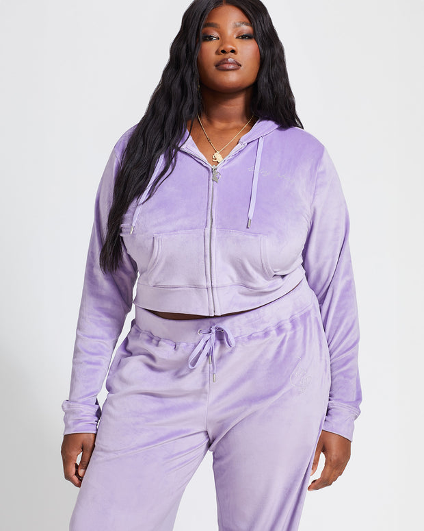 Plus sized model shown wearing lavender velour zip up hoodie with matching wide leg sweatpants. Zippered sweatshirt features rhinestone Baby Phat script logo on upper chest and oversized rhinestone cat logo on the back. Sweatshirt features silver cat logo zipper pull.