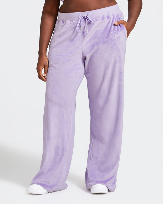 Plus sized model shown wearing light purple velour sweatpants. Pants feature a wide leg, open bottom fit with a rhinestone Baby Phat cat logo on the wearer's left upper thigh. Pants feature pockets and an elastic waistband with a drawstring tie.