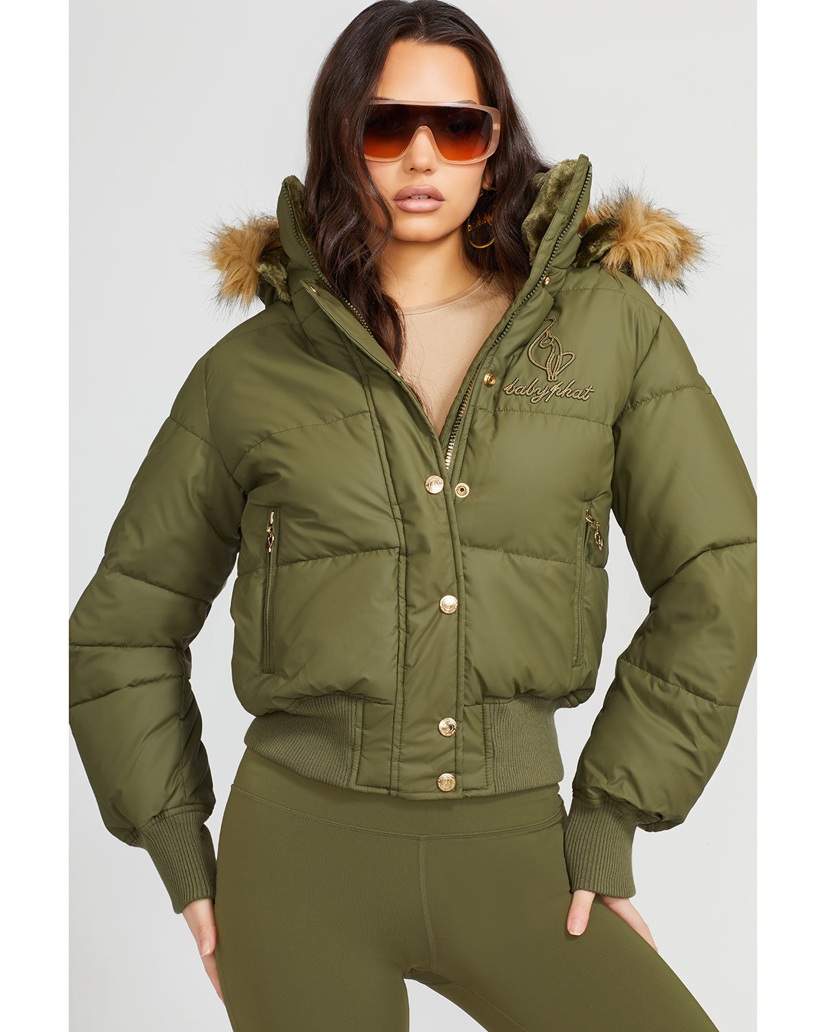 Model shown wearing olive green puffer jacket. Coat features faux fur detachable hood and Baby Phat script logo on front chest and oversized cat logo on the back. Jacket also features gold cat logo zipper pulls on the front pockets and center front.