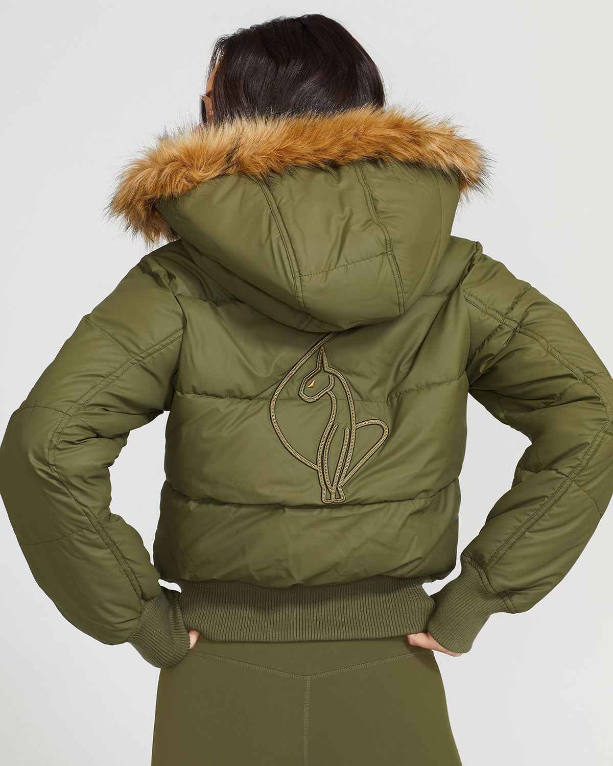 Model shown wearing olive green puffer jacket. Coat features faux fur detachable hood and Baby Phat script logo on front chest and oversized cat logo on the back. Jacket also features gold cat logo zipper pulls on the front pockets and center front.