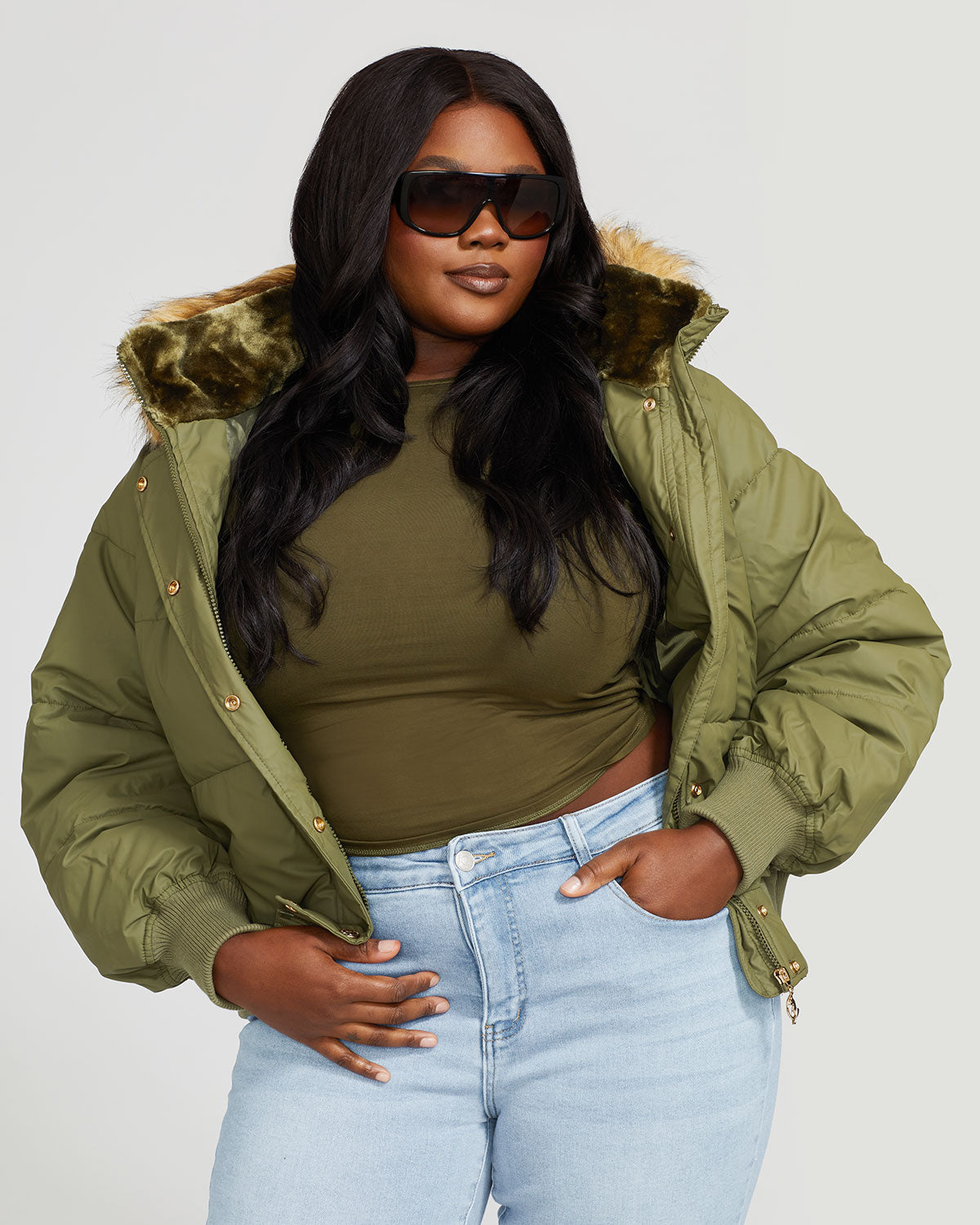 Plus sized model shown wearing olive green puffer jacket. Coat features faux fur detachable hood and Baby Phat script logo on front chest and oversized cat logo on the back. Jacket also features gold cat logo zipper pulls on the front pockets and center front.