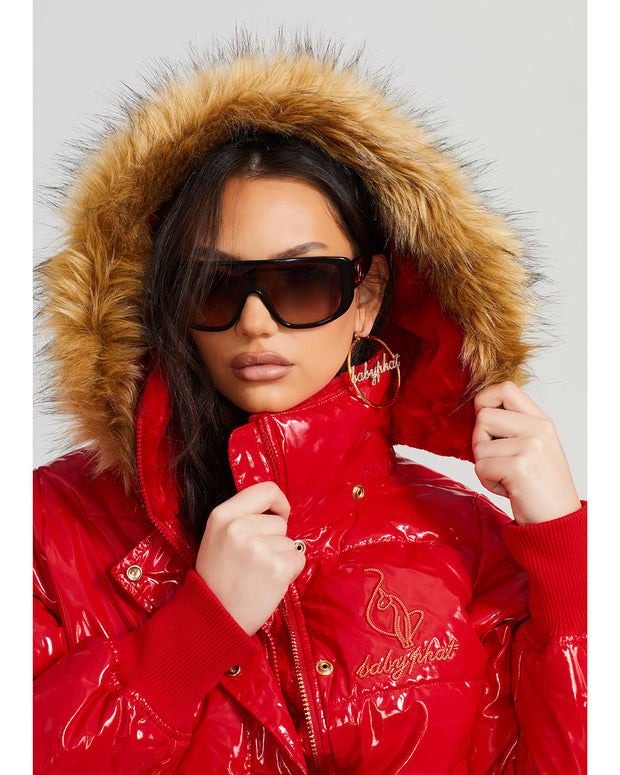 Model shown wearing glossy red puffer jacket. Coat features natural faux fur trimmed detachable hood and Baby Phat script logo on front chest and oversized cat logo on the back. Jacket also features gold cat logo zipper pulls on the front pockets and center front.