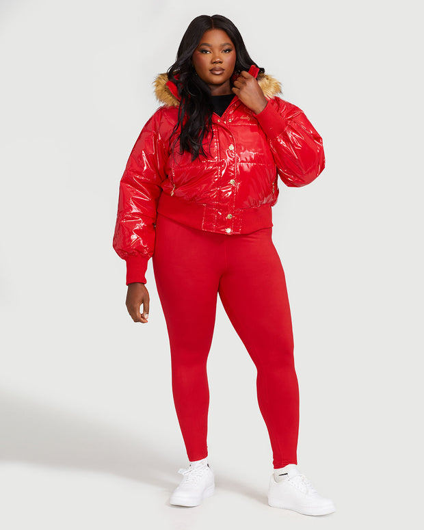 Plus sized model shown wearing glossy red puffer jacket. Coat features natural faux fur trimmed detachable hood and Baby Phat script logo on front chest and oversized cat logo on the back. Jacket also features gold cat logo zipper pulls on the front pockets and center front.