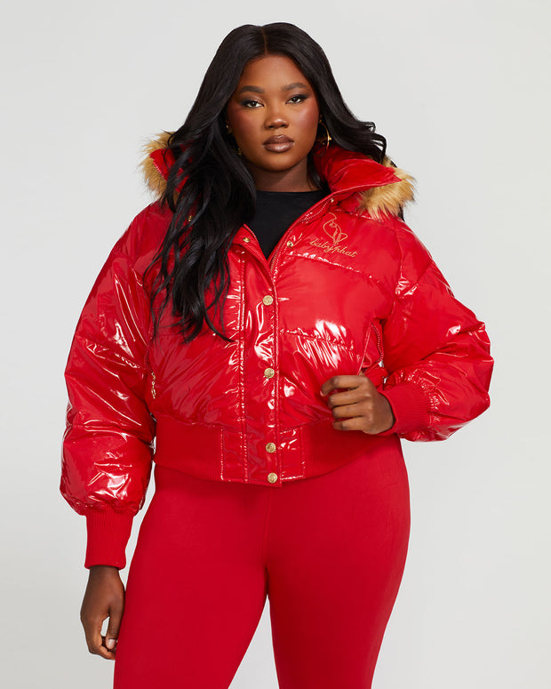 Plus sized model shown wearing glossy red puffer jacket. Coat features natural faux fur trimmed detachable hood and Baby Phat script logo on front chest and oversized cat logo on the back. Jacket also features gold cat logo zipper pulls on the front pockets and center front.