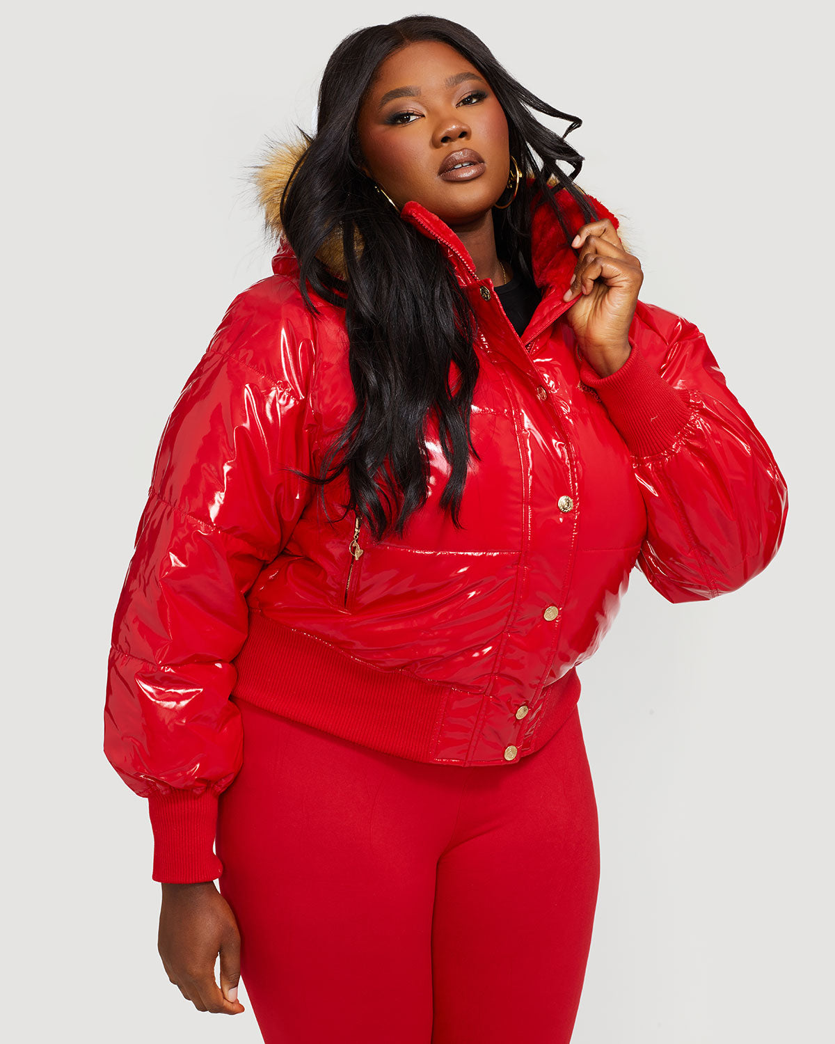 Plus sized model shown wearing glossy red puffer jacket. Coat features natural faux fur trimmed detachable hood and Baby Phat script logo on front chest and oversized cat logo on the back. Jacket also features gold cat logo zipper pulls on the front pockets and center front.