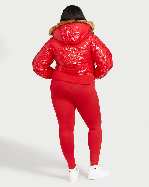 Plus sized model shown wearing glossy red puffer jacket. Coat features natural faux fur trimmed detachable hood and Baby Phat script logo on front chest and oversized cat logo on the back. Jacket also features gold cat logo zipper pulls on the front pockets and center front.