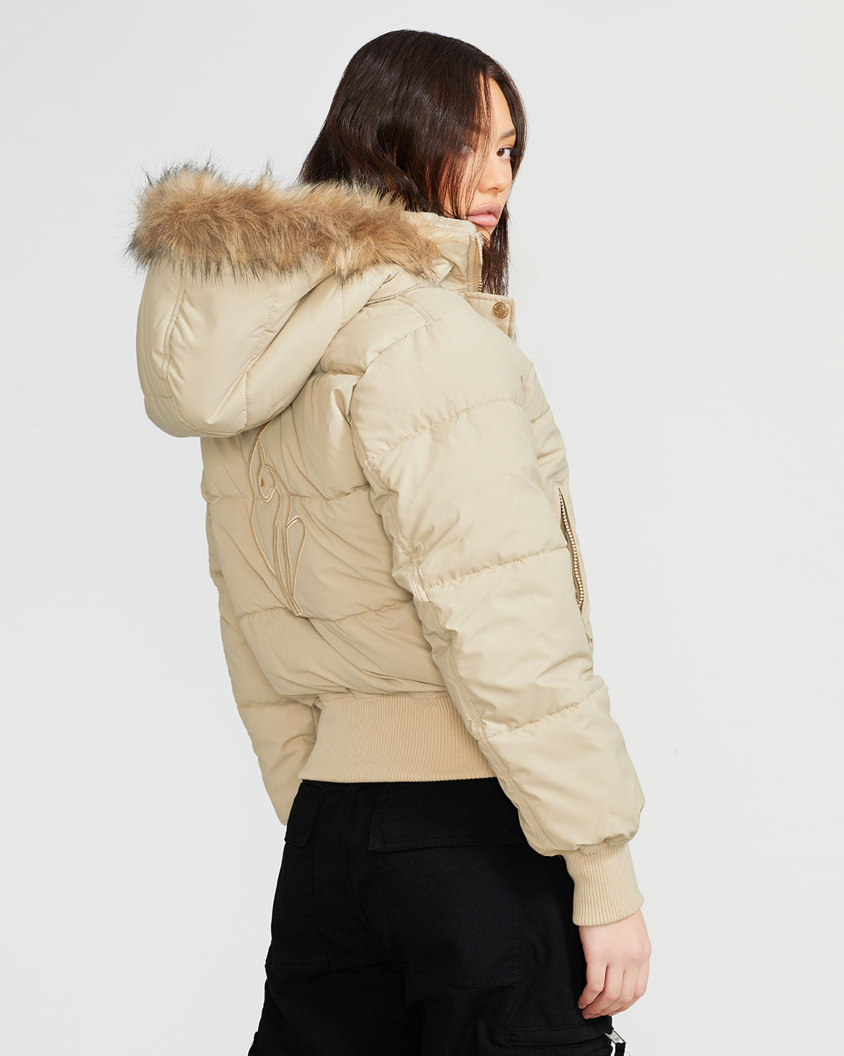 Model shown wearing light tan puffer jacket. Coat features natural faux fur trimmed detachable hood and Baby Phat script logo on front chest and oversized cat logo on the back. Jacket also features gold cat logo zipper pulls on the front pockets and center front.