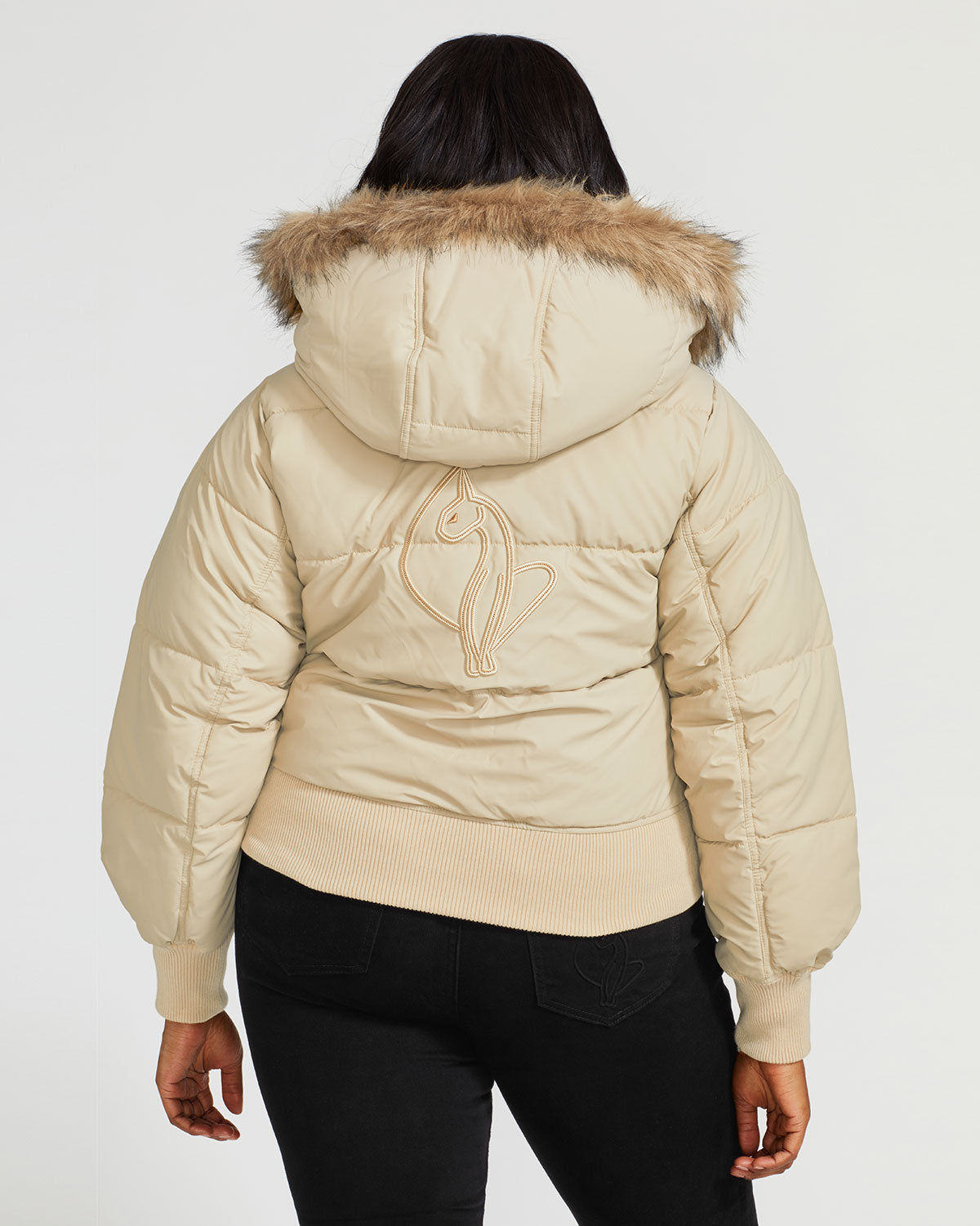 Plus sized model shown wearing light tan puffer jacket. Coat features natural faux fur trimmed detachable hood and Baby Phat script logo on front chest and oversized cat logo on the back. Jacket also features gold cat logo zipper pulls on the front pockets and center front.