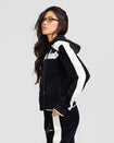 Size view image of standard sized model shown wearing black velour zip up hoodie with color blocked off white panel down both sleeves. Zippered sweatshirt features off white Baby Phat script logo across upper chest and oversized solid cat logo on wearer's right front. Sweatshirt features black ribbing at the wrists and hem that has off white tipping. Model is wearing matching black sweatpants with off white color blocking.