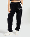 Standard sized model shown wearing black velour sweatpant with color blocked cream stripe down both sides. Sweatpant features embroidered Baby Phat script and cat logo on wearer's upper left thigh. Model has her hand in her pocket.