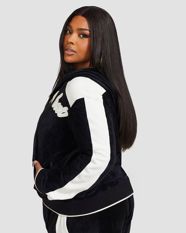 Side view image of plus sized model wearing black velour zip up hoodie with color blocked off white panel down both sleeves. Zippered sweatshirt features matching black ribbing at the wrists and hem with off white tipping. Model is also wearing matching black sweatpant with off white color blocking. 