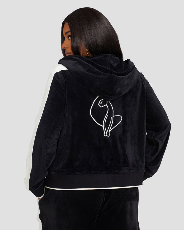 Back view image of plus sized model wearing black velour zip up hoodie with color blocked off white panel down both sleeves. Zippered sweatshirt features matching black ribbing at the wrists and hem with off white tipping. Large embroidered cat logo on center back. Model is also wearing matching black sweatpant with off white color blocking. 