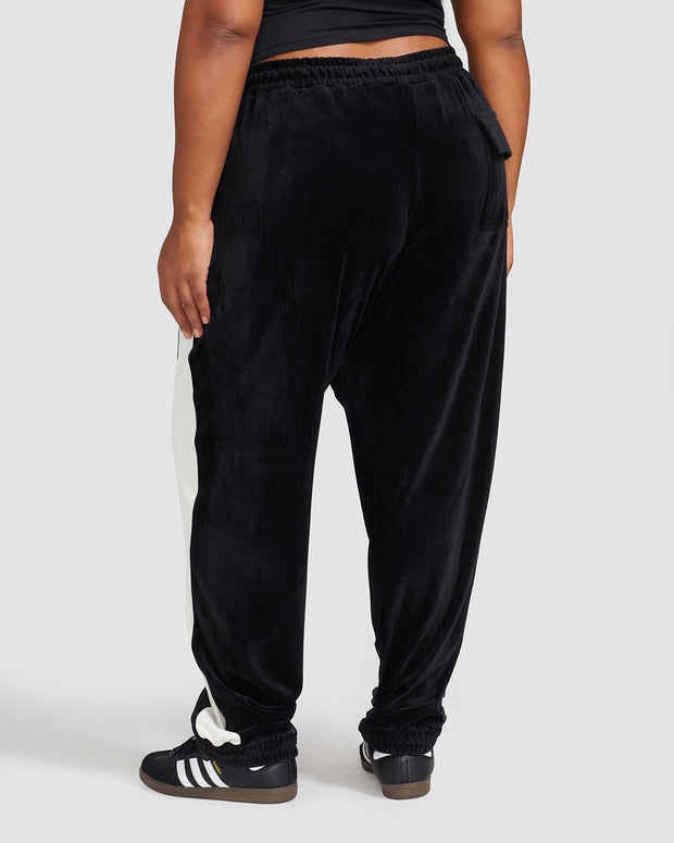 Back view image of plus sized model wearing black velour sweatpant with color blocked cream stripe down both sides. Sweatpant features oversized flap pocket on rear right side.