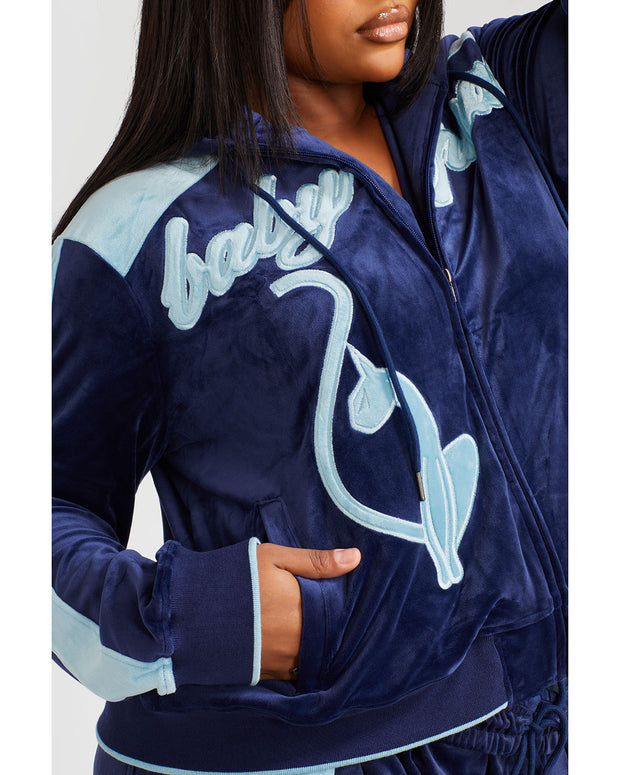 Detail image shows plus sized model wearing navy blue velour zip up hoodie with color blocked light blue panel down both sleeves. Zippered sweatshirt features light blue Baby Phat script logo across upper chest and oversized solid cat logo on wearer's right front.