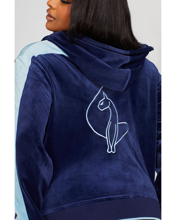 Back view image of plus sized model wearing navy blue velour zip up hoodie with color blocked light blue panel down both sleeves. Zippered sweatshirt features matching navy blue ribbing at the wrists and hem with light blue tipping. Large embroidered cat logo on center back. 